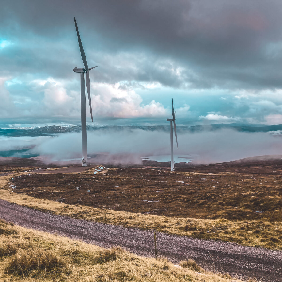 Two wind turbines against a dramatic sky with low cloud